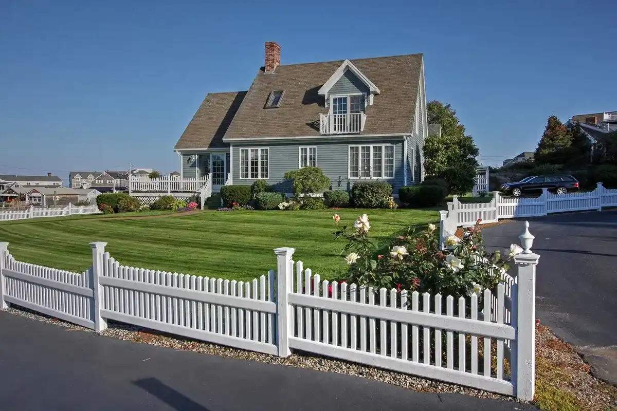 White picket fence in front of a home with a green lawn