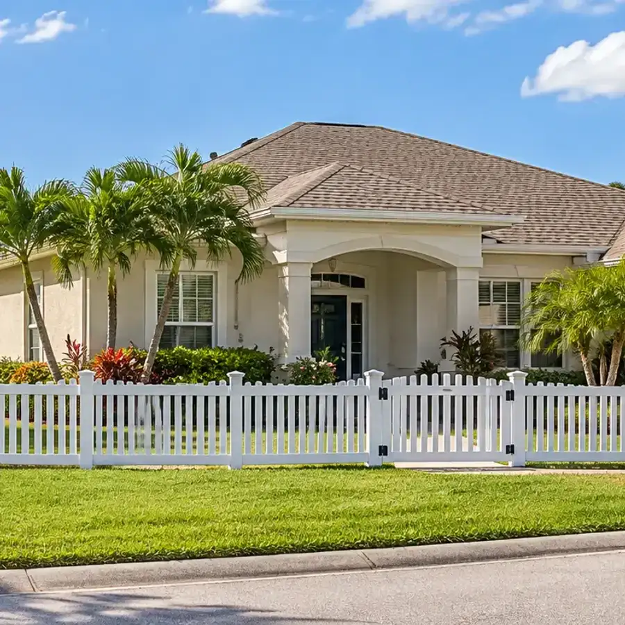 Florida stucco home with palm trees and a white vinyl picket fence with a gate